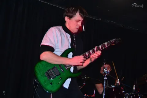Guitarist with a green electric guitar on stage.